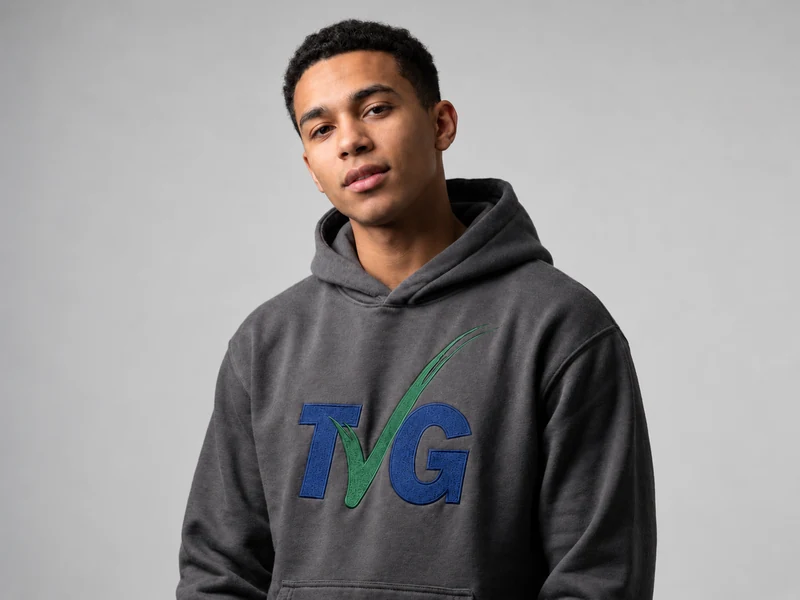 Illustrative portrait of a model wearing a charcoal hoodie with embroidered TVG branding